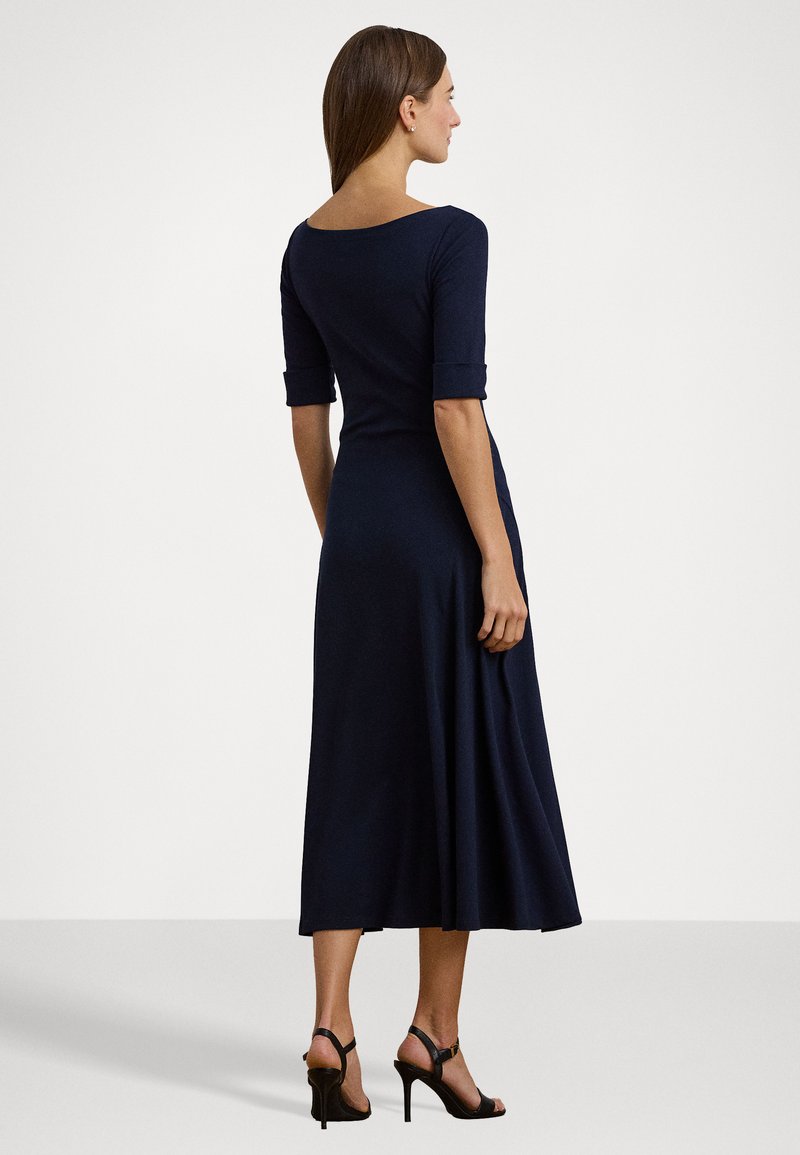 Robe bleu marine, longueur genou avec un dos dégagé, manches trois-quarts et jupe évasée. Une paire de talons noirs à lanières.