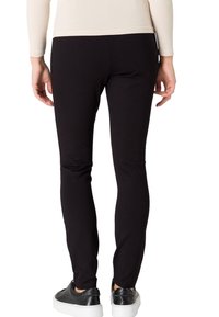 Leggings noirs en tissu extensible, design près du corps, sans coutures visibles, associés à des baskets noires avec une semelle blanche.