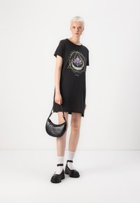 Svart t-shirt klänning med en grafisk lotusdesign, kortärmad och med avslappnad passform. Parat med en svart perforerad handväska och kraftiga skor.