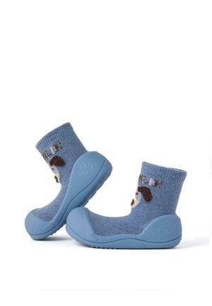 Calcetines de tela azul con suelas de goma, que presentan un diseño de un perro marrón y blanco y la palabra "Charlie" tejida en el puño. Textura suave.