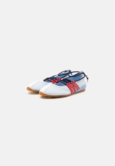 Paire de chaussures blanches décontractées à lacets avec des accents bleu marine et rouge et des semelles en caoutchouc marron sur fond uni.