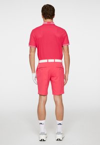 Rosa polotröja med vita detaljer, matchad med shorts i samma färg. Vitt bälte och handskar fulländar outfiten. Enkel, sportig design.