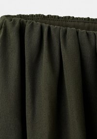 Tissu côtelé vert olive foncé rassemblé à une taille élastique, montrant la texture et les plis.