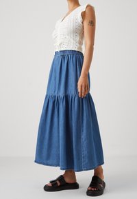 Vit ögonblus med volangärmar, i kombination med en lång blå denimkjol med ett lagerdesign. Svarta platta sandaler fulländar looken.