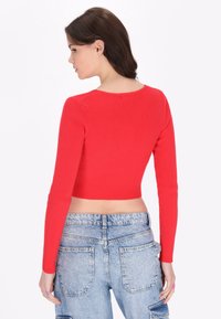 Piros bordázott crop top hosszú ujjakkal, kerek nyakkivágással, fitted kialakítással és sima textúrával, amelyet világoskék farmernadrággal párosítanak.