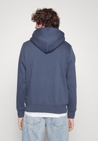 Felpa con cappuccio blu navy realizzata in tessuto morbido, caratterizzata da una vestibilità comoda, polsini a costine e una tasca a marsupio sul davanti.