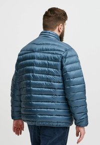 Matinis teal pūkinis švarkas su siuvinėta tekstūra, stovinčia apykakle ir elastiniais rankogaliais. Yra slapta užtrauktuko uždarymo sistema ir laisvas siluetas.