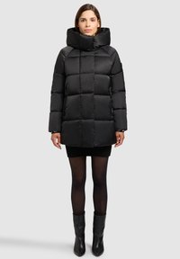 Geacă matlasată neagră, cu guler înalt, prevăzută cu buzunare laterale cu fermoar și finisaj neted, lucios. Lungime sub genunchi.