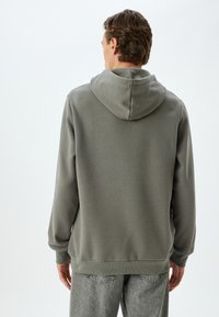 Sudadera gris con una textura suave, que cuenta con una gran capucha, puños y dobladillo acanalados, combinada con unos vaqueros claros, ajustados.