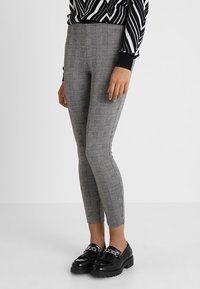 Gray and black checked leggings with a slim fit, featuring a high waist and made from stretchy fabric, paired with black loafers.
