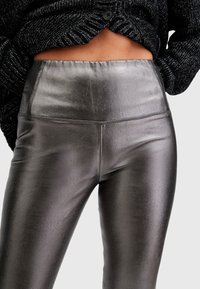 Leggings argento metallizzato con vita alta e superficie liscia. I dettagli delle cuciture sono visibili lungo le cuciture.