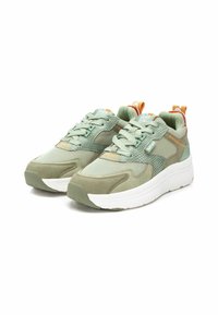 Zapatillas verde claro que combinan malla y ante, con una suela blanca elevada y detalles naranjas en el talón.