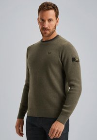 Olivgrüner gestrickter Pullover mit gerippten Ärmelbündchen und Saum, ausgestattet mit einem schwarz akzentuierten Patch an den Ärmeln und einem runden Ausschnitt.
