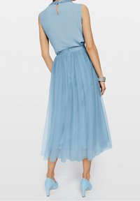 Lichtblauwe jurk met een mouwloze top, doorschijnende gelaagde rok en een sleutelgatdetail op de rug. Aangekleed met een bijpassende riem en hakken.