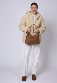 Borsa a tracolla in pelle marrone con silhouette arrotondata e dettagli in oro. Cappotto teddy beige testurizzato con cappuccio e grandi bottoni.