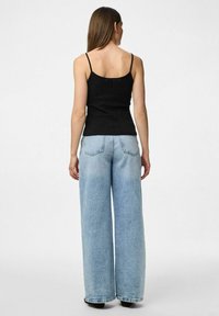 Un débardeur noir à côtes associé à un jean large bleu clair, avec une taille haute et des poches arrière, présenté de dos.