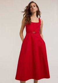 Rochie roșie fără mâneci din țesătură de bumbac, cu decolteu pătrat, siluetă în formă de A, buzunare laterale și o curea decorativă cu cataramă metalică.