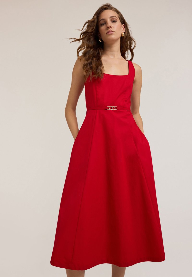 Rochie roșie fără mâneci din țesătură de bumbac, cu decolteu pătrat, siluetă în formă de A, buzunare laterale și o curea decorativă cu cataramă metalică.
