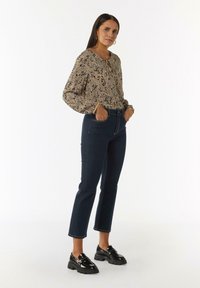Bloes met bloemenprint en lange mouwen, gecombineerd met donkerdenim jeans en zwarte platform loafers. Opvallende texturen en patronen zichtbaar.