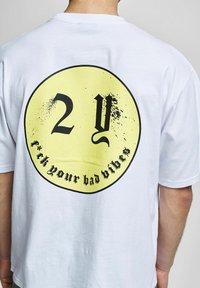 Biała koszulka z krótkim rękawem z dużą żółtą okrągłą grafiką na plecach. Tekst na czarno: "2Y f*ck your bad vibes" z efektem przetarcia.