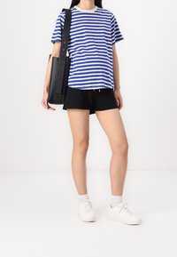 Camiseta a rayas azul y blanca, pantalones cortos negros y zapatillas blancas. Bolso de hombro con una correa larga. La tela parece suave, con un ajuste casual.