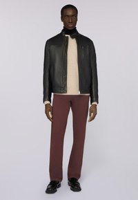 Černá kožená bunda s vysokým límcem, béžový svetr pod ní, burgundské kalhoty a černé boty s lesklým povrchem.