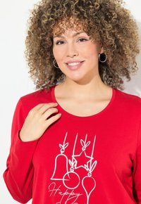 Rode langemouw T-shirt met witte grafische prints van bellen, een ster en ornamenten met de tekst "Happy." Zacht materiaal, ronde hals.