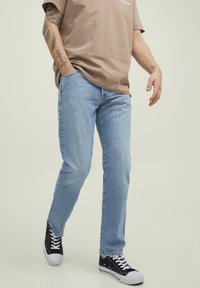 Light blue denim jeans with a straight fit, completed with black sneakers and a brown t-shirt. Features visible stitching and pockets.