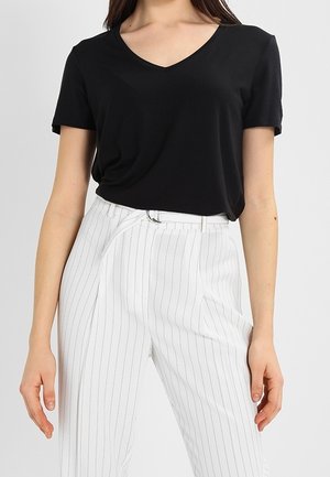 Czarny t-shirt z dekoltem w serek o luźnym kroju, zestawiony z białymi spodniami w cienkie paski. Materiał t-shirtu wydaje się miękki i gładki, spodnie mają dopasowany, szyty fason.