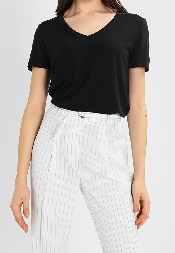 T-shirt noir col V à coupe décontractée, associé à un pantalon blanc à fines rayures. Le tissu du t-shirt semble doux et lisse, le pantalon présente une coupe ajustée.
