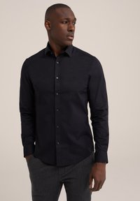 Chemise noire à boutons avec un col structuré et des manches longues, fabriquée dans un tissu lisse, avec des boutons assortis et une coupe ajustée.