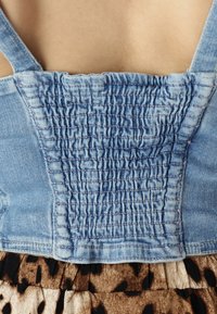 Top din denim cu spate smockat și bretele, asortat cu o fustă cu un model maro și negru. Accent pe textura țesăturii și detaliile designului.