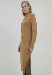 Rochie tricotată de culoare cămilă, cu guler înalt, mâneci lungi, slit lateral și manșete cu textură ribbed. Textură moale, design ajustat și stil de lungime medie.