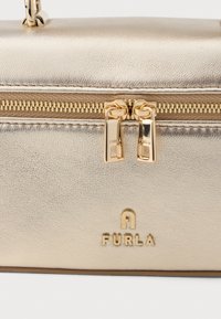 Zeltaini metāla ādas soma ar rāvējslēdzēja aizdari, diviem zeltainiem aparatūras elementiem, iefočētu zīmola nosaukumu "FURLA" un gludu teksturētu apdari.