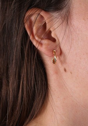 Boucles d'oreilles couleur or avec un design fluide et ondulé. Elles épousent le lobe de l'oreille et présentent une texture lisse et brillante. Esthétique simple et épurée.