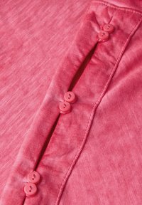 Pink button-up shirt with a textured fabric, featuring six round, pink buttons along the front opening and contrasting stitching details.