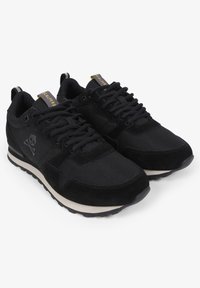 Zwarte sportieve schoenen van suede en stof, met een doodshoofdlogo, een gestructureerde bovenkant, platte veters en een contrasterende crèmekleurige zool.