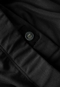 Svart stoff med en jevn tekstur, synlige sømmer og en metallisk knapp som aksent. Knappen har fire hull og en blank overflate.