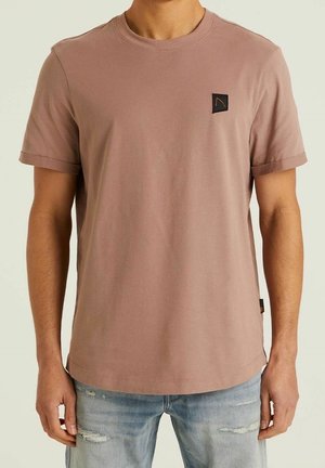 T-shirt z krótkim rękawem w luźnym kroju, wykonany z bawełnianego materiału w kolorze przybrudzonego różu, z małą czarną naszywką z logo na klatce piersiowej oraz podwiniętymi mankietami.