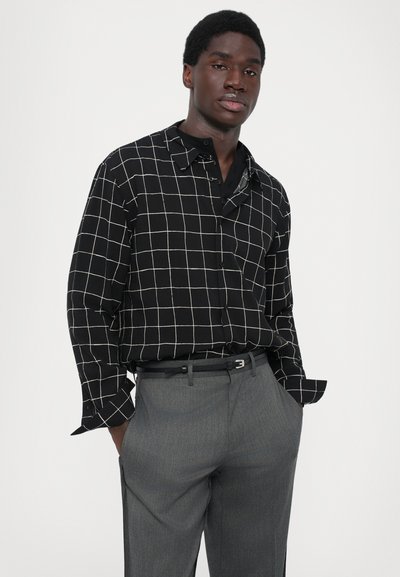 Zwarte geblokte overhemd met wit rasterpatroon, lange mouwen, met knoopkraag. Gecombineerd met grijze op maat gemaakte broek en een zwarte riem.