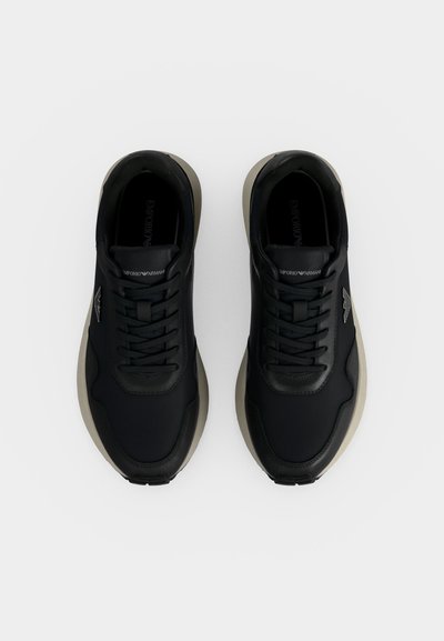 Paire de baskets noires Emporio Armani avec semelles beiges vues de dessus sur fond blanc.