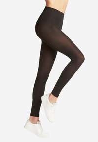 Zwarte leggings met een hoge tailleband, gemaakt van rekbare stof; een gladde textuur en een aansluitend ontwerp, gecombineerd met witte sportschoenen.