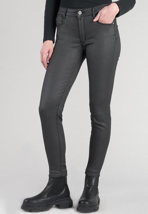 Vaqueros negros de corte slim, hechos de un material suave, con bolsillos frontales, cremallera y detalles de costura en contraste. Combinados con botas negras.