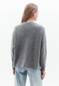 Maglione grigio a costine con una vestibilità boxy, caratterizzato da una trama diagonale e un orlo arrotondato. Abbinato a pantaloni lucidi di un blu chiaro.
