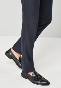 Sötétkék, slim fit nadrág, oldalt fekete csíkkal, fekete bőr, bojtos részletekkel ellátott mokaszinokkal párosítva.