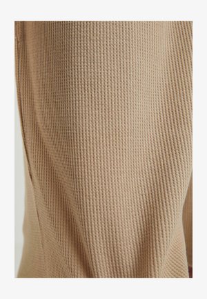 Beige teksturert stoff med et ribbet mønster, som viser et mykt og lett materiale egnet for hverdagsbruk.