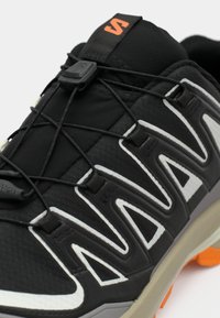 Black and gray athletic shoe with orange accents, featuring a quick-lace system and a textured sole for outdoor use.