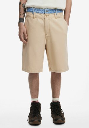 Beige cargo shorts with a relaxed fit, featuring a blue patterned belt. Worn with brown hiking shoes and white socks with red stripes.