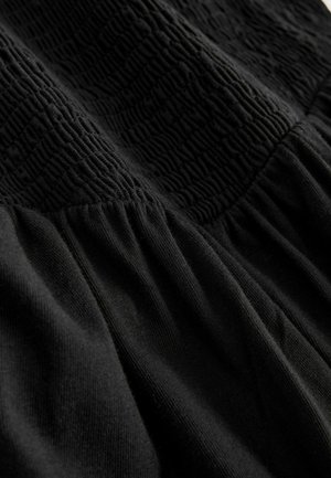 Schwarzes Kleid mit strukturierter Brustpartie, geraffter Taille und glattem, fließendem Rock. Hergestellt aus weichem, leichtem Stoff.