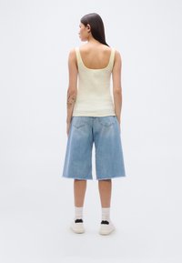 Ανοιχτό κίτρινο τοπ χωρίς μανίκια με τετράγωνο ντεκολτέ συνδυασμένο με άνετες μπλε denim culottes. Το μοντέλο φοράει λευκά αθλητικά παπούτσια και κοντές κάλτσες.